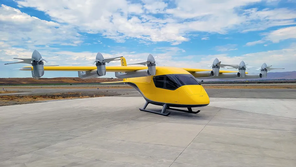 Yellow and white Wisk Gen 6 eVTOL with a row of propellers on its long wing, parked on a ramp